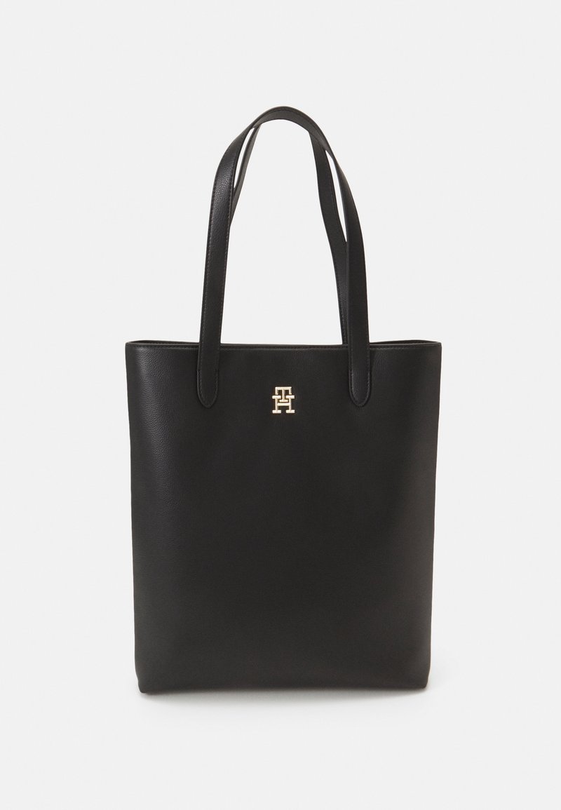 Sac à tote en cuir noir avec deux longues poignées, texture lisse, design minimaliste et accent logo doré à l'avant.