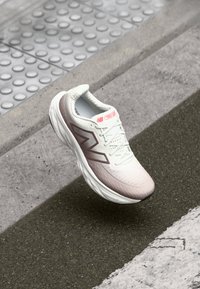 Chaussure de course légère en blanc et rose pâle avec un dessus texturé, présentant un logo latéral proéminent et une semelle rembourrée pour le confort.