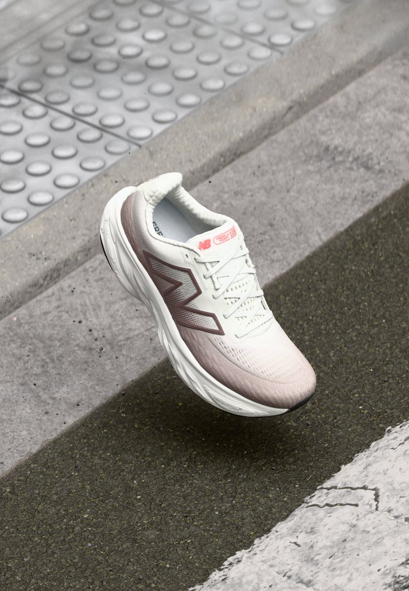 Chaussure de course légère en blanc et rose pâle avec un dessus texturé, présentant un logo latéral proéminent et une semelle rembourrée pour le confort.