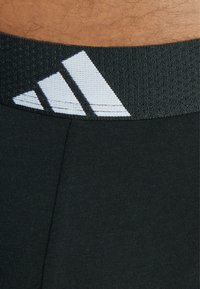 Svarta sportshorts med ett texturerat midjeband och en vit tre-stripes-logotyp. Materialet verkar slätt och åtsittande.