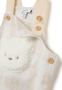 Romper lavorato a maglia beige con applicazione di orsetto di peluche crema, bottoni in legno e bretelle testurizzate. Progettato per neonati, presenta un materiale morbido e accogliente.