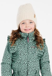 Groene winterjas met een patroon, ruches en een capuchon, met een ritssluiting en een roze ritslip. Het kind draagt een crèmekleurige gebreide muts.