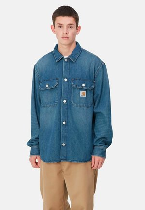 Camicia di jeans di blu medio, con due tasche frontali con patte, chiusura a bottoni e vestibilità rilassata. Texture morbida e design casual.