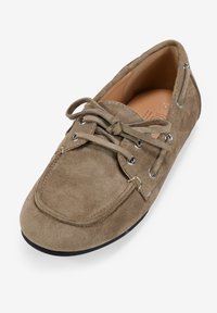 Zapato de ante en marrón claro con punta redonda. Presenta cordones de imitación de cuero, ojales de metal y una parte superior texturizada. Suela de goma negra.