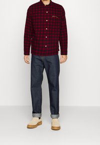 Camicia di flanella a quadri rossi e neri con chiusura a bottoni, abbinata a jeans scuri e stivali Chelsea beige.