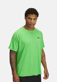 Camiseta atlética verde de manga corta con un acabado texturizado y mangas raglán. Presenta un pequeño logo negro en la parte frontal.