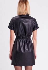 Robe courte en cuir noir à manches courtes, taille cintrée, texture lisse et design simple, avec manches retroussées et ourlet droit.