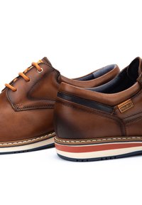 Zapatos de cuero marrón con cordones naranjas, acentuados por un panel azul marino oscuro. Presenta una suela contrastante blanca y roja con detalles de costura.