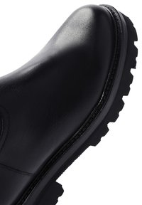 Black leather boot with a rounded toe, textured surface, and rugged black sole featuring deep treads for traction. Seam detailing at the edge.