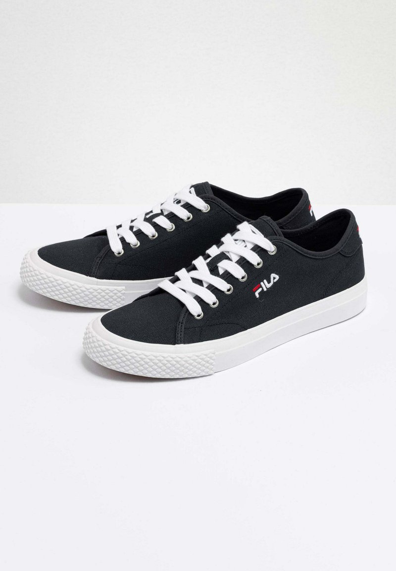 Zapatillas de lona negras con cordones blancos y suela de goma. Presentan un detalle de logo en rojo en el lateral y una suela blanca texturizada.