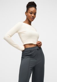 Εκρού κοντομάνικη ριμπ μπλούζα με μακρύ μανίκι, σε συνδυασμό με ψηλόμεσο σκούρο γκρι παντελόνι με πιέτες μπροστά και πλαϊνές τσέπες.