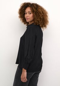 Schwarze Bluse mit langen �Ärmeln und kragenförmigem Halsausschnitt, mit Gathered-Ärmeln und entspannter Passform, kombiniert mit dunkelgrauen Jeans.