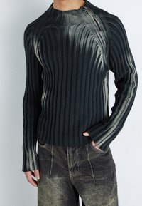 Mörkgrå ribbad stickad tröja med hög hals och långa ärmar, med en subtil gradienteffekt och synliga sömmar. Avslappnad passform.