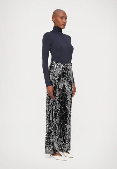 Un pulover turtleneck din lână albastru închis cu mânecă lungă, asortat cu o pereche de pantaloni cu paiete argintii și talie înaltă, creând o silueta elegant�ă. Tocuri albe cu vârf ascuțit.