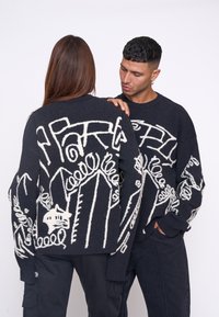 Pulover negru cu modele abstracte albe, are mâneci lungi, guler rotund și un finisaj texturat. Modelele sunt variate și intricate.