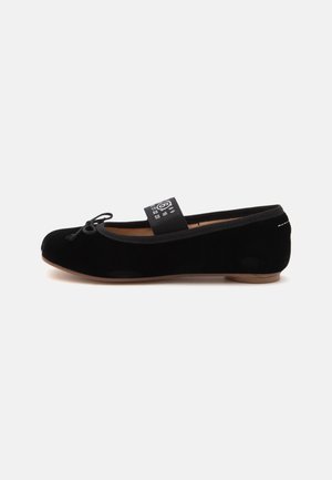 Ballerine en velours noir avec un petit nœud sur l’orteil et une bride élastique noire avec des chiffres blancs sur le dessus.