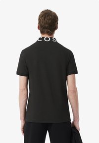 Svart polo-t-shirt med en kontrasterande vit stickad krage som har "COS" logotypen. Kortärmad, slät textur, minimalistisk design.