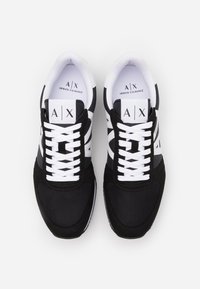 Svart og hvit treningstøvel laget av mesh og suede materiale, med teksturert tå, hvite snører, og et "A/X"-logo på tungen.