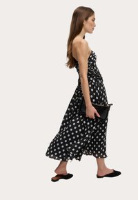Sort kjole med prikker, fitted bodice, flagrende nederdel og rynkede detaljer. Båret med en sort clutch og slip-on sko.