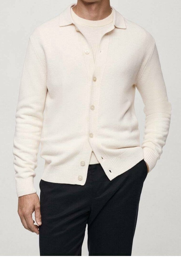 Cream-colored cardigan made of soft knit fabric, featuring a collared neck, button front, and ribbed cuffs. Worn over a light top.