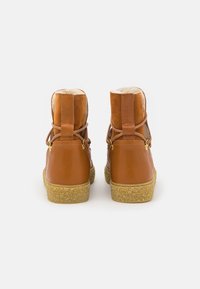 Botas de tobillo de cuero marrón con acentos de ante, forro suave y suela de goma con acabado texturizado. Correas ajustables en la parte trasera.