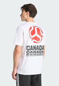 Camiseta de algodón blanca con un gran gráfico rojo y texto negro repetido que dice "CANADÁ" en la parte de atrás. Mangas cortas y cuello redondo.