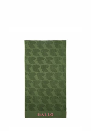 Asciugamano verde con un motivo ripetuto di teste stilizzate, con il testo rosa "GALLO" in basso. Tessuto morbido e texturizzato.