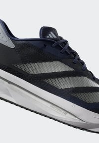 Námornícky modré a čierne bežecké tenisky so sivými pruhmi, biele stredové podrážky s označením "Lightstrike Pro" a námornícke šnúrky na svetlom pozadí.