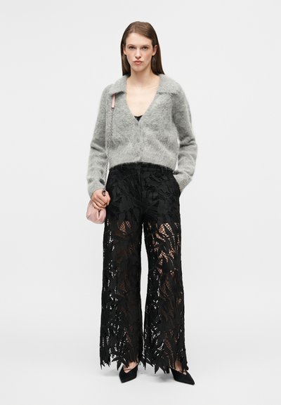 Cardigan en mohair gris clair avec un col en V et des boutons à l'avant, associé à un pantalon large en dentelle noire avec des découpes florales, chaussures noires pointues.