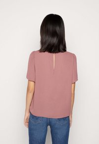 Krátký rukáv, lehký top v barvě jemné růžové s měkkou texturou. Obsahuje klíčovou díru na zádech, volný střih a zaoblený lem.