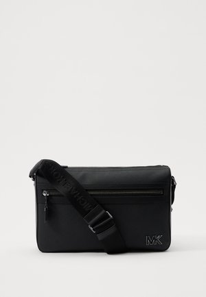 Black crossbody bag with a textured exterior, featuring a front zip pocket, adjustable strap, and embossed logo. Rectangular shape.