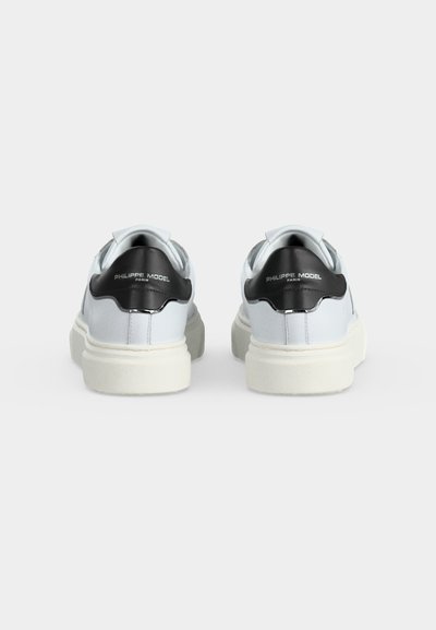 Paire de baskets blanches vues de dos, avec des languettes noires au talon affichant le texte "Philippe Model Paris", sur fond uni.
