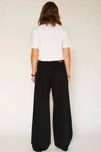 Pantalon large noir en denim à taille haute, associé à un t-shirt blanc uni, vu de dos. Comprend deux poches arrière.