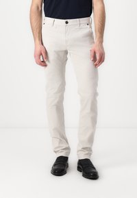 Helle beige Slim-Fit-Hosen aus Baumwolle. Mit Gürtelschlaufen, Taschen vorne und einem Knopfverschluss. Glatte Textur, minimales Design.