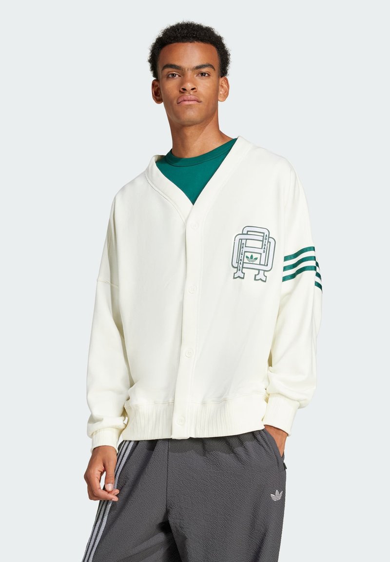 Krämfärgad kofta med knappar, v-ringad hals, ribbade muddar och tre gröna ränder på ärmarna. Har en grafisk logotyp på framsidan.