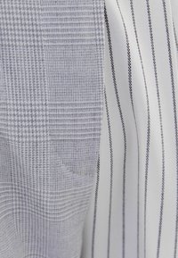 Košile na knoflíky s texturovaným šedým a bílým kostkovaným vzorem na jedné straně a vertikálními pruhy na druhé, s hladkým povrchem látky.