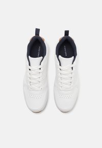 White leather sneakers with a smooth texture, featuring a navy interior and brown accents on the heel and tongue. Closed with white laces.