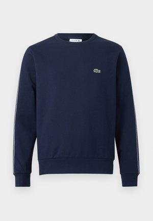 Felpa girocollo blu navy con maniche lunghe, polsini costellati e piccolo logo verde a forma di coccodrillo sul petto.