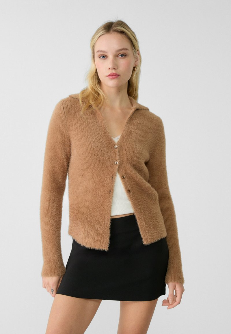 Brauner, fusseliger Cardigan mit V-Ausschnitt, Knopfverschluss, langen Ärmeln und einer weichen Textur, kombiniert mit einem schwarzen Minirock.