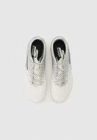 Chaussures de soccer blanches avec une finition lisse, présentant des accents argentés, un design à lacets et une zone texturée près de l'orteil pour une meilleure adhérence.