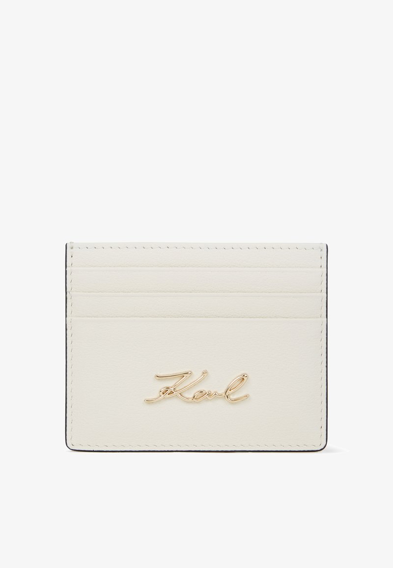 Skórzana kieszonka na karty w kolorze off-white z złotym napisem "Karl". Posiada cztery sloty na karty, gładką teksturę oraz minimalistyczny design z czarnymi krawędziami.
