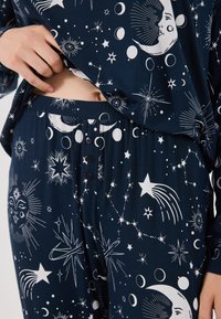 Ensemble de pyjama bleu marine en tissu doux avec des motifs célestes blancs, incluant des étoiles, des lunes et des soleils, et un détail de boutons sur le pantalon.