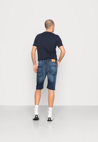 Farkkuhousut, joissa on haalistunut sininen pesu, keskipituiset reiteen asti, yhdistetty mustan t-paidan ja valkoisten korkeakorkoisten tennareiden kanssa, joissa on mustia yksityiskohtia.