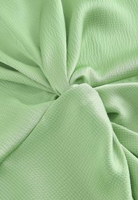 Tissu vert clair et doux avec un motif texturé subtil, légèrement froncé et torsadé au centre.