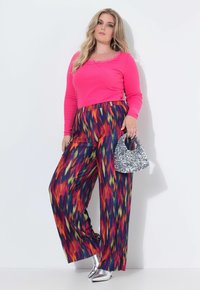 Top de manga larga de canalé rosa con borde de encaje, combinado con pantalones anchos de patrones multicolores y un bolso plateado brillante. Zapatos plateados de punta.