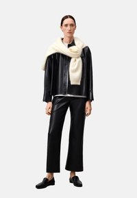 Schwarze Leder-oversized-Jacke, schwarze Leder-weite Hose, weiße Wollschal lässig über die Schultern drapiert, schlichtes weißes T-Shirt darunter.