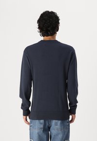 Pulover tricotat de culoare albastru marin, cu mâneci lungi, guler și tiv cu aspect zimțat. Textură netedă, croială dreaptă și design minimalist.