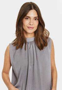 Top senza maniche in morbido tessuto grigio con scollatura alta e dettaglio arricciato. Texture liscia e vestibilità comoda, adatta per un abbigliamento casual.