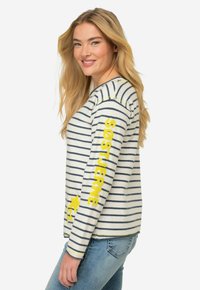 Maglione a maniche lunghe a righe in crema e blu navy con testo giallo. Tessuto a maglia, scollatura rotonda e vestibilità rilassata. Presenta un logo sulla manica.