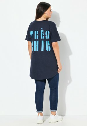 Námořnická oversized tričko s potiskem "TRÈS CHIC" v světle modré, kulatým výstřihem, krátkými rukávy a zakřiveným lemem. V kombinaci s modrými skinny džíny.